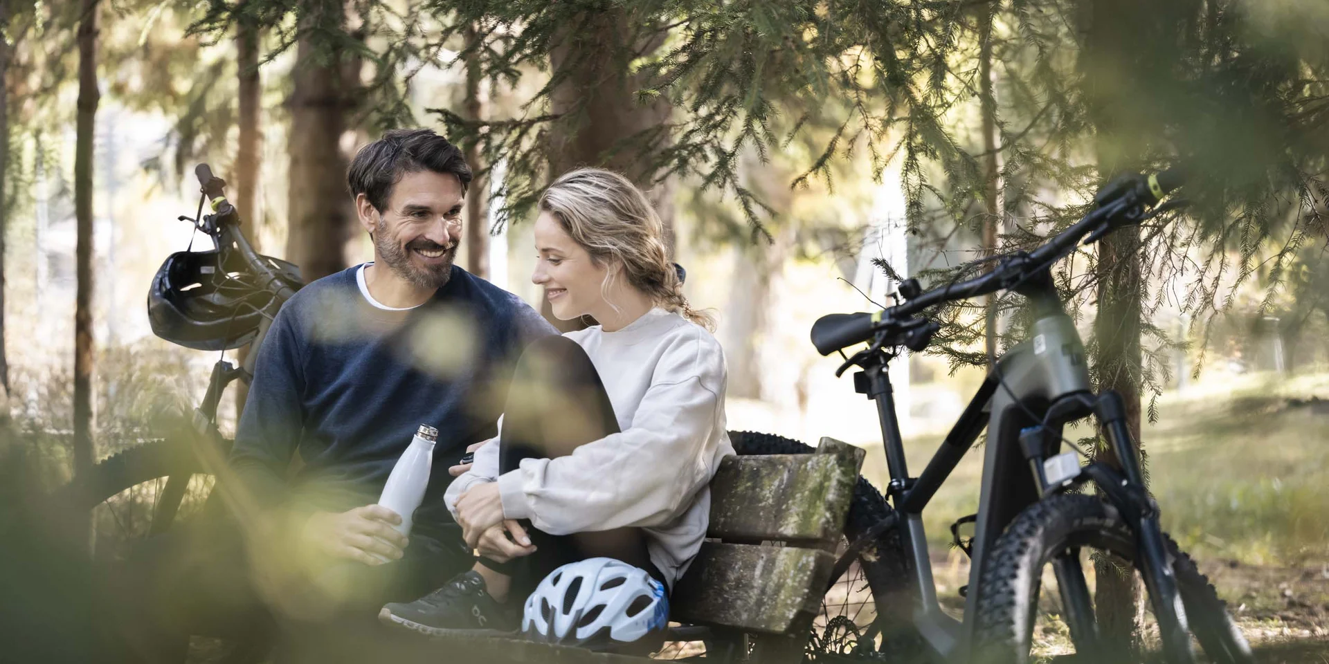 Couple resting on a bench in the forest with bicycles nearby