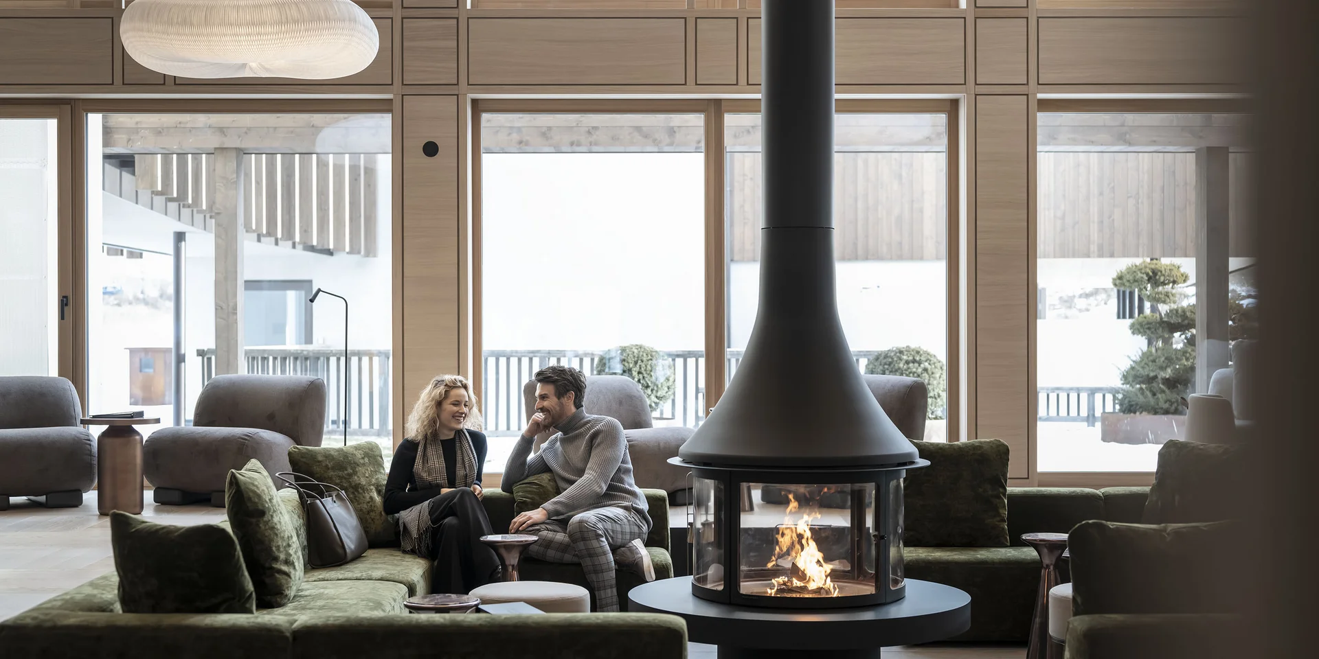 Coppia seduta su divano verde davanti a caminetto moderno in soggiorno luminoso