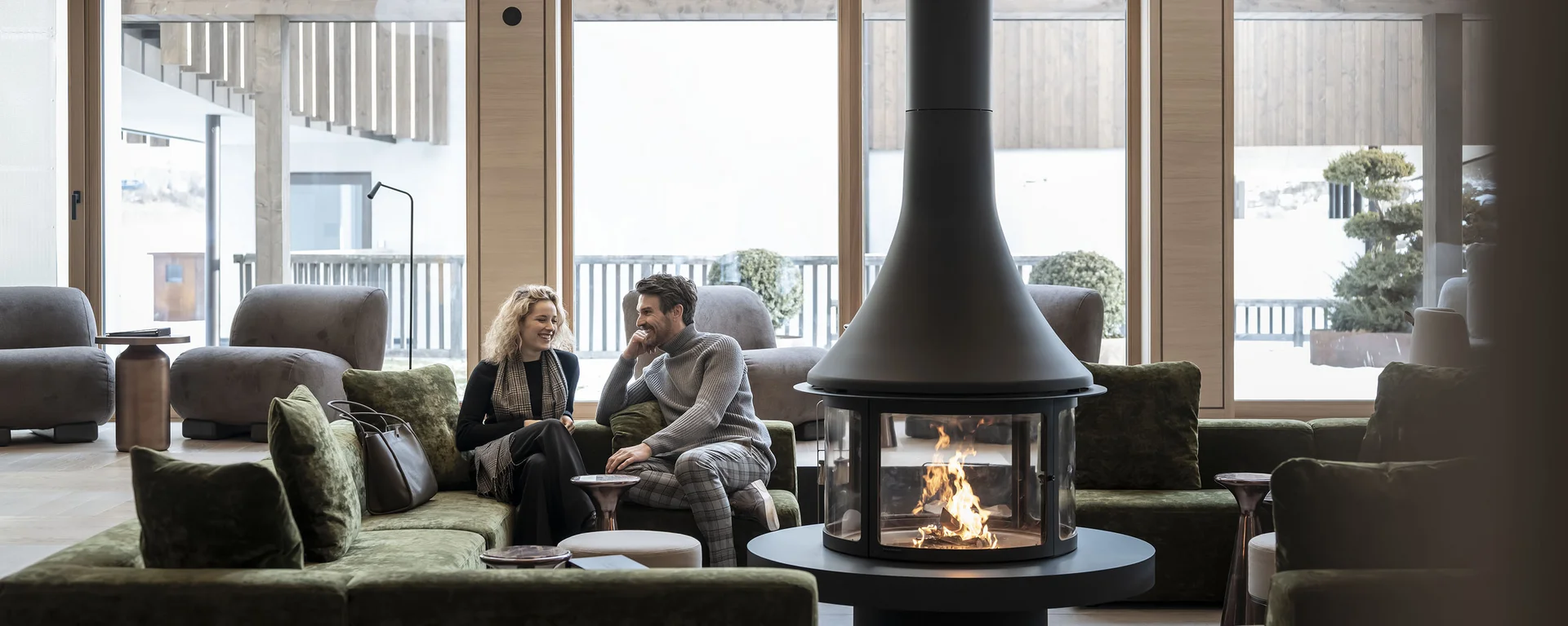 Paar sitzt auf grünem Sofa vor modernem Holzofen in hellem Wohnzimmer