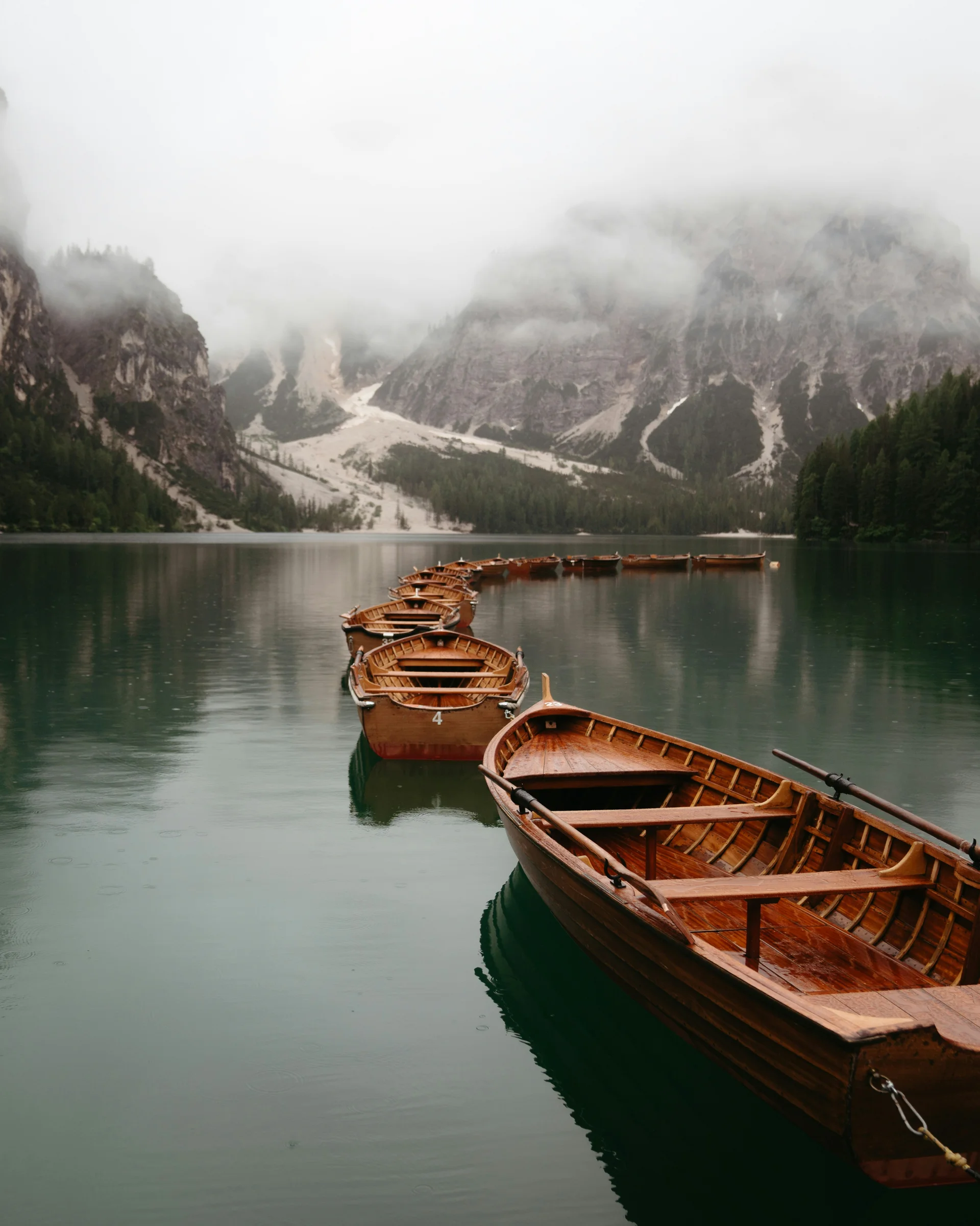 Reihe von Holzbooten auf einem See vor nebligen Bergen