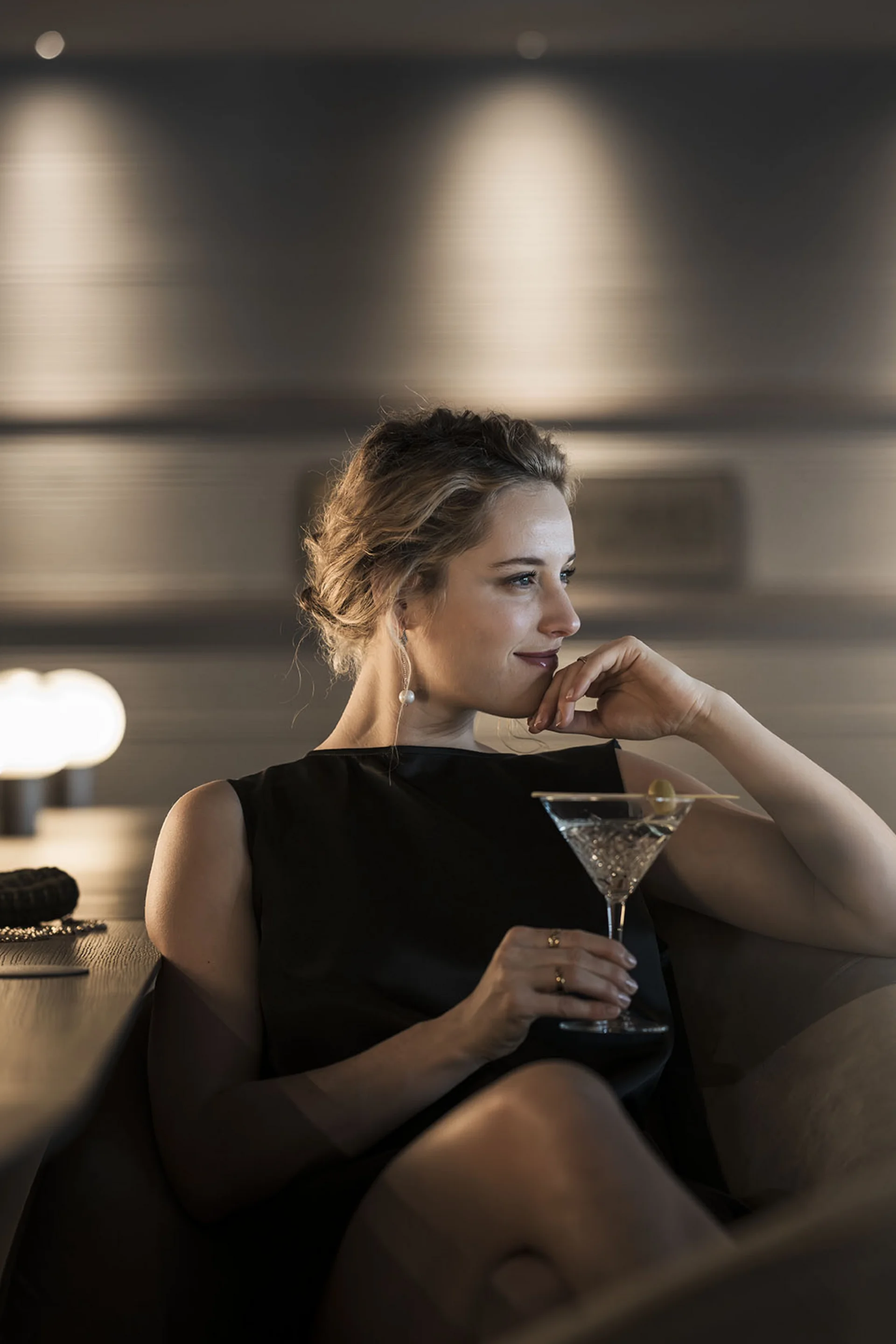 Frau in schwarzem Kleid entspannt mit Cocktail in schicker Bar