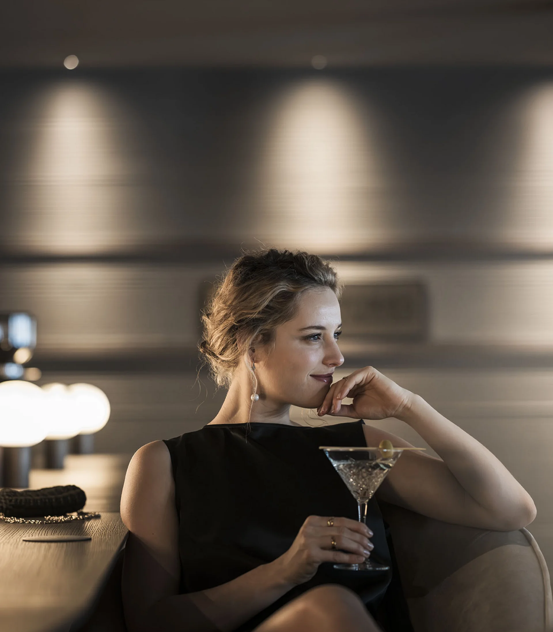 Donna in abito nero rilassata con cocktail in elegante bar