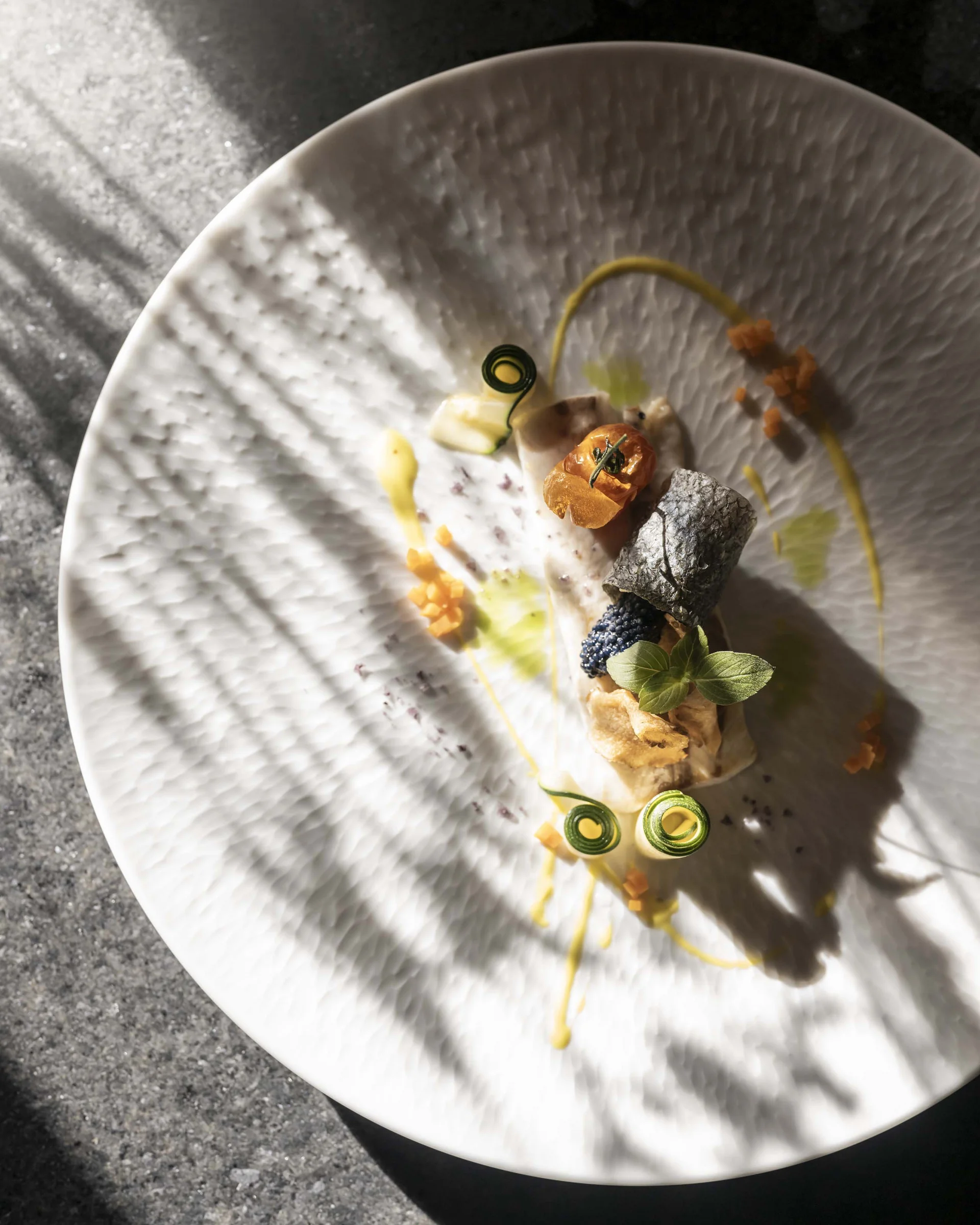 Fein angerichtetes Gourmetgericht auf weißem Teller mit Kräutern und Soße