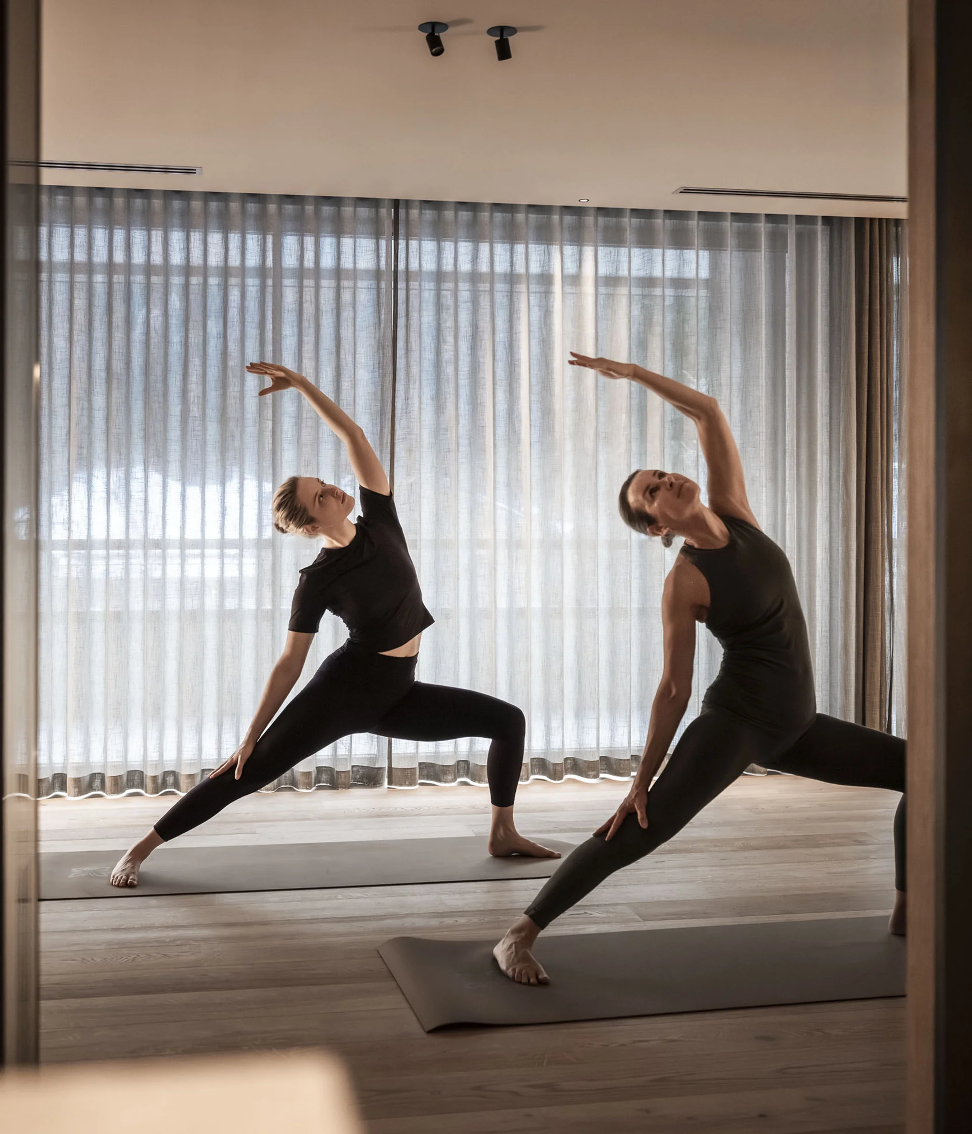 Two women practicing yoga on mats in a bright room