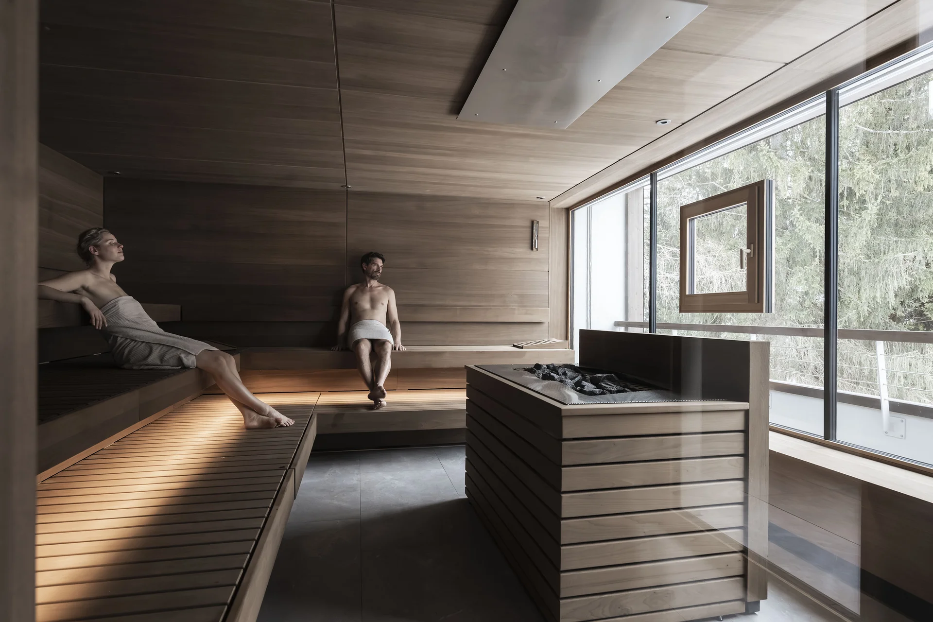 Zwei Personen entspannen in einer holzverkleideten Sauna mit Blick ins Freie