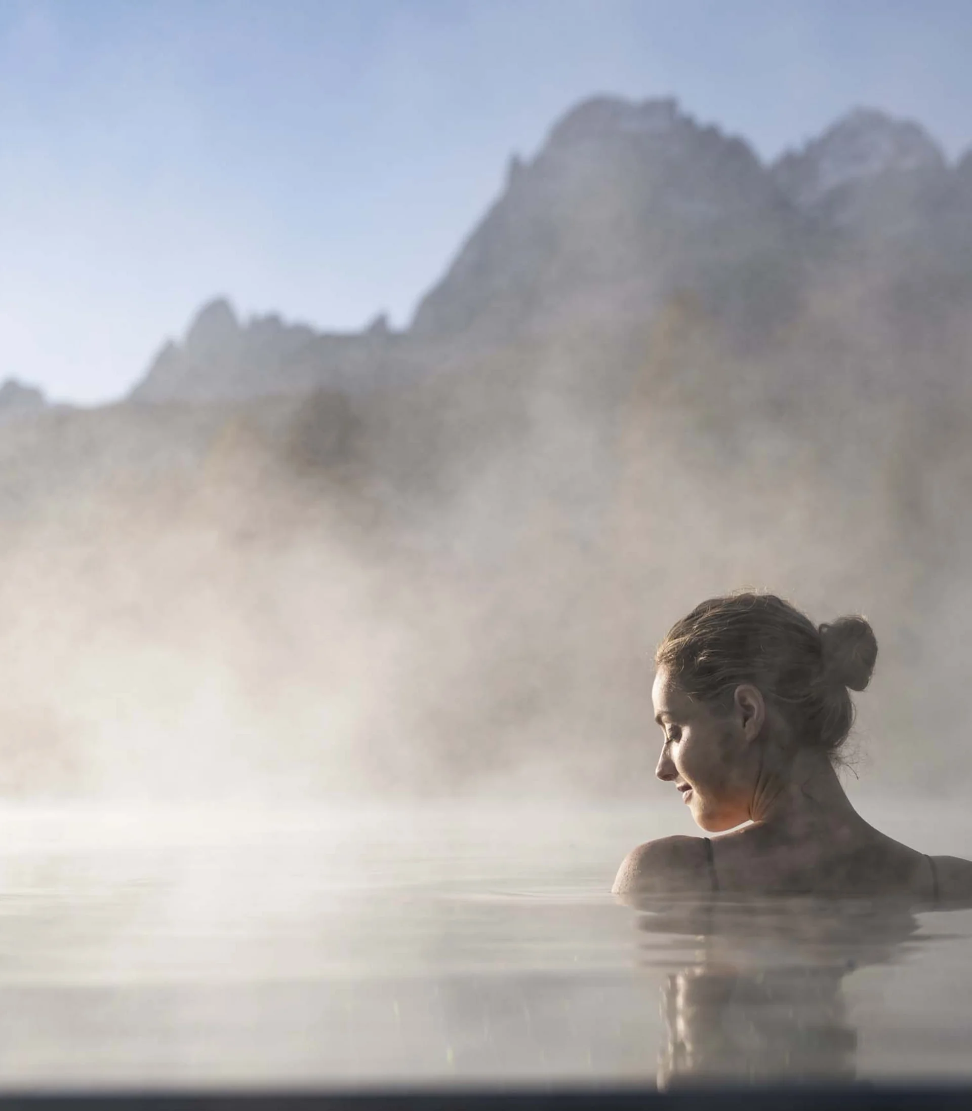 Frau entspannt im dampfenden Thermalbad mit Bergblick