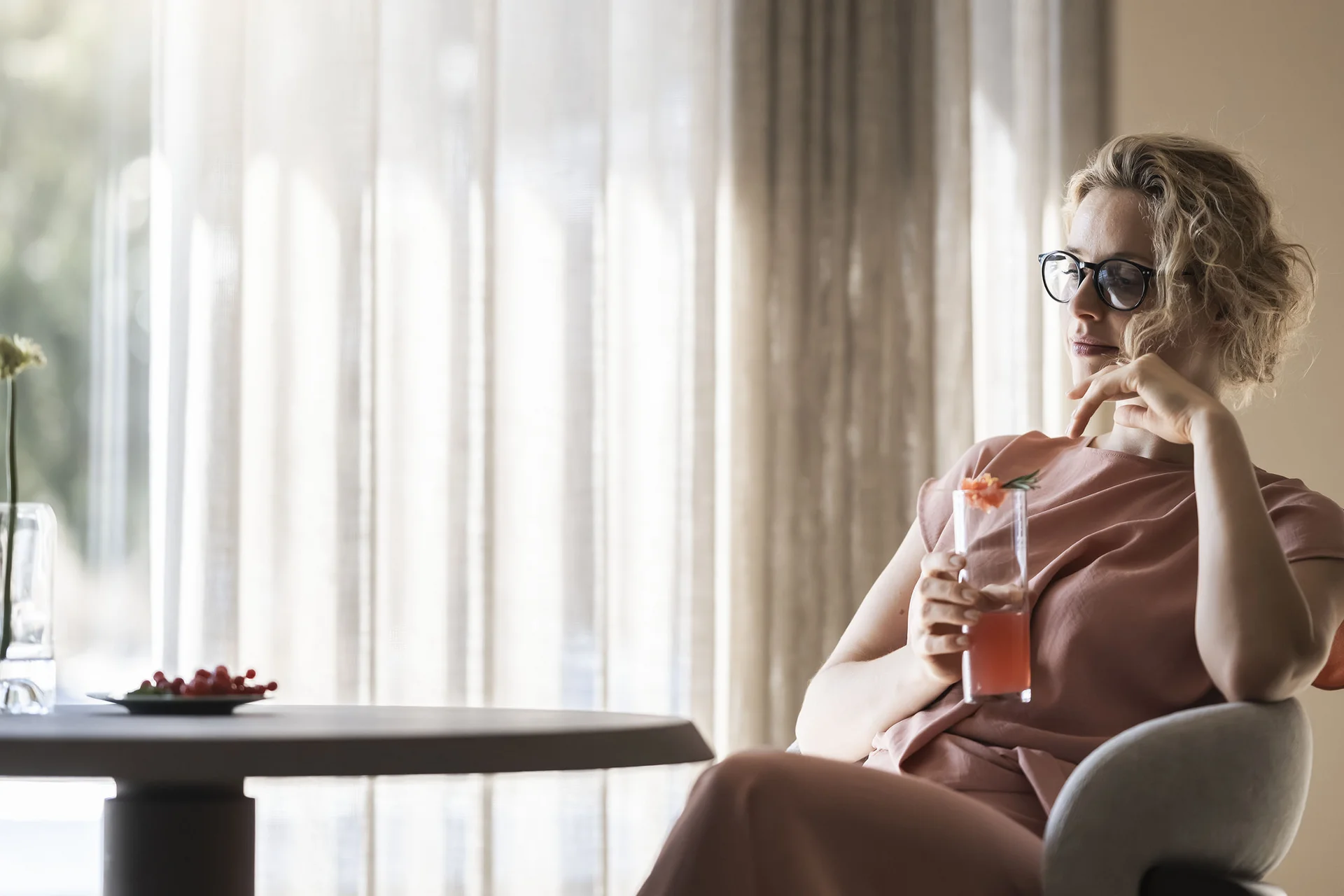 Woman with glasses sitting alone drinking juice in a bright room