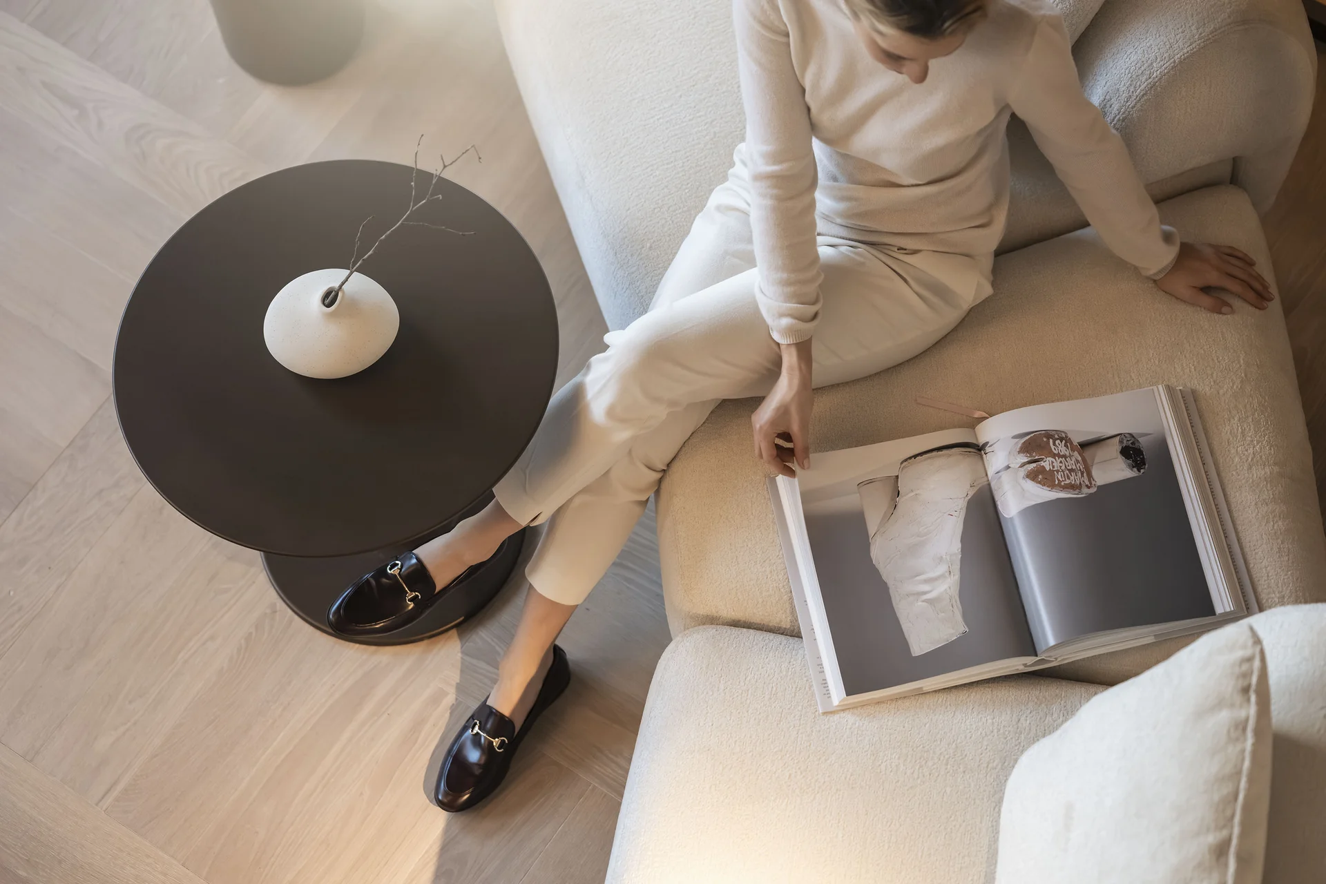 Frau sitzt auf Sofa und blättert in einem Magazin neben einem Tisch mit Vase