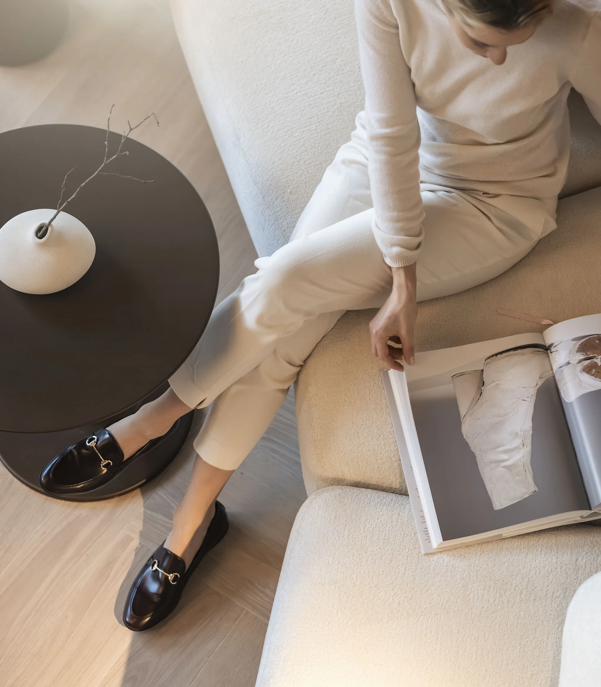 Donna seduta sul divano che sfoglia una rivista accanto a un tavolo con vaso