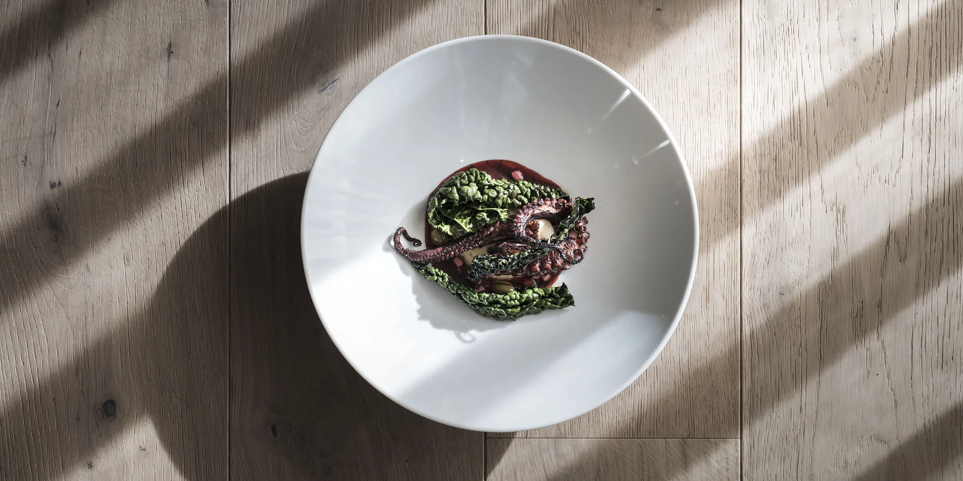 Polpo grigliato con foglie di cavolo su piatto bianco