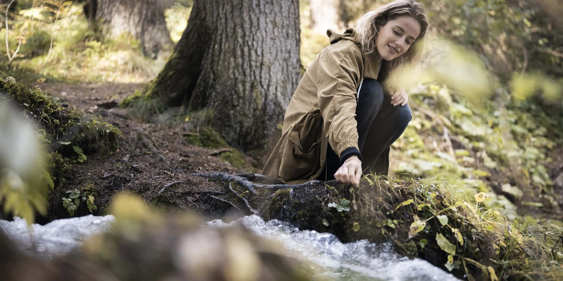 Frau sitzt am Waldrand und berührt Wasser eines Baches