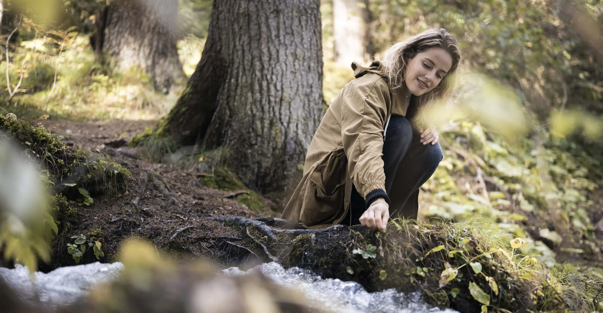Frau sitzt am Waldrand und berührt Wasser eines Baches