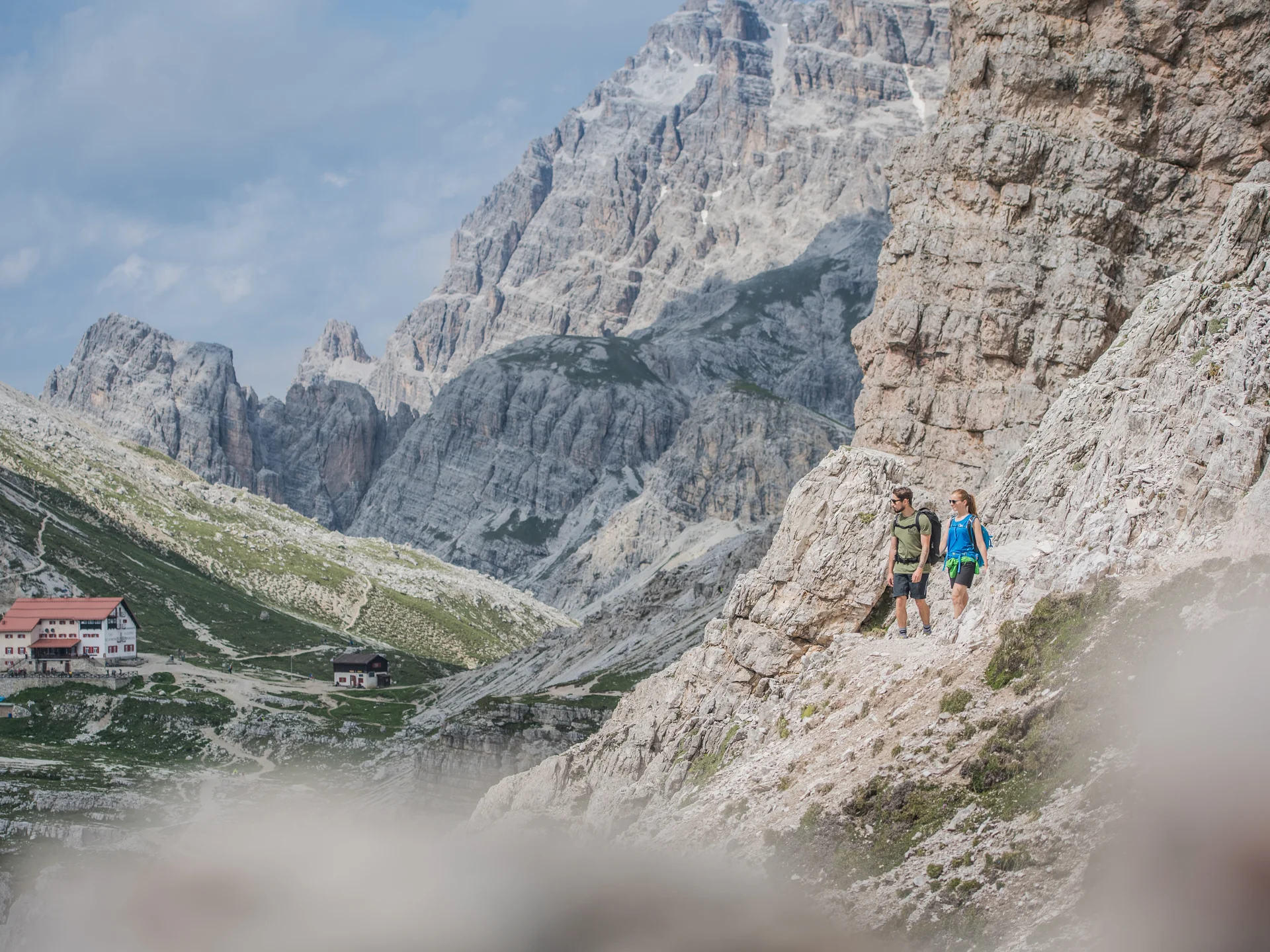 Ihr Hotel an den Drei Zinnen: das Monika in Sexten Zwei Wanderer auf einem felsigen Pfad in den Bergen mit Berghütten im Tal