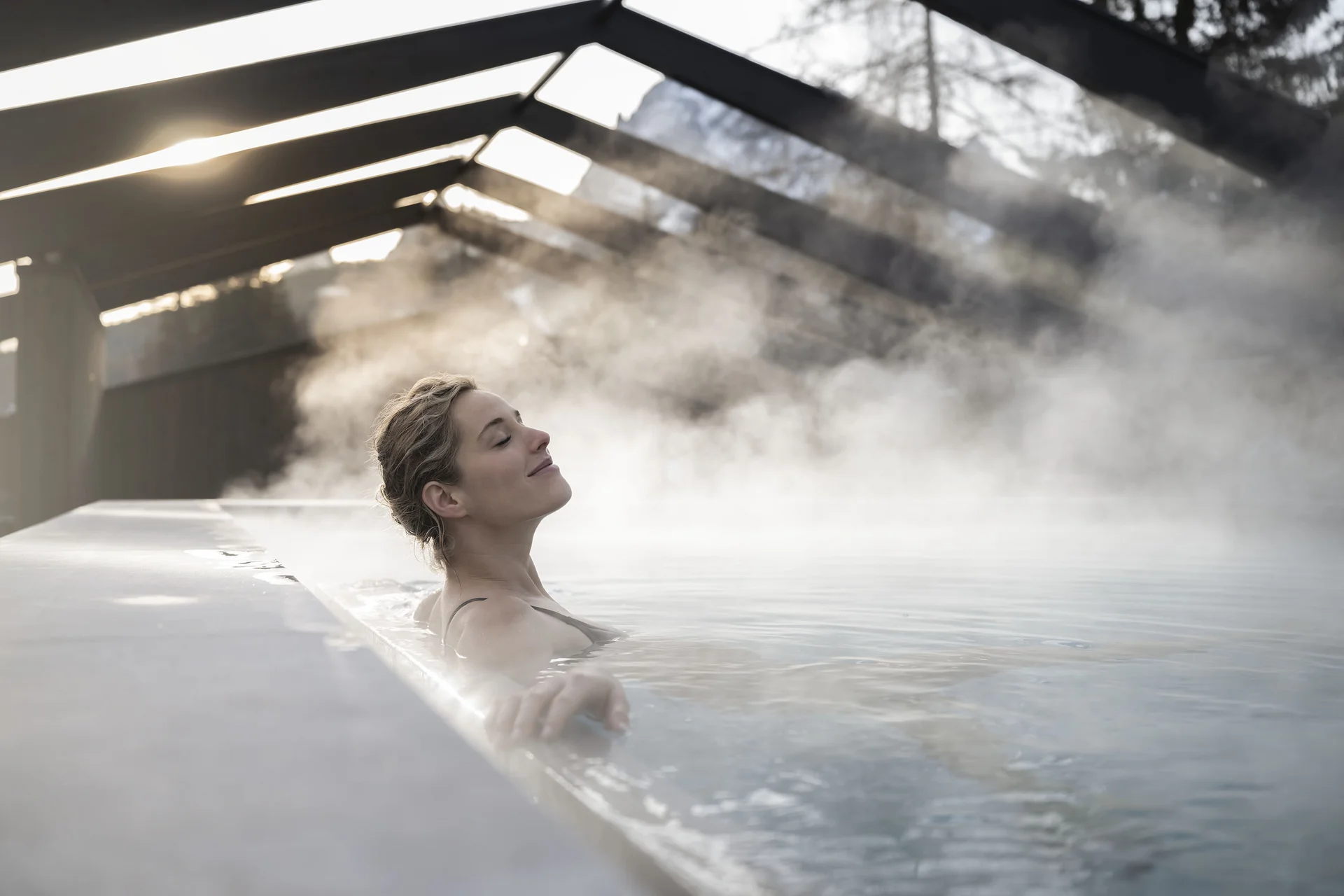 Woman relaxing in steaming thermal pool under glass roof