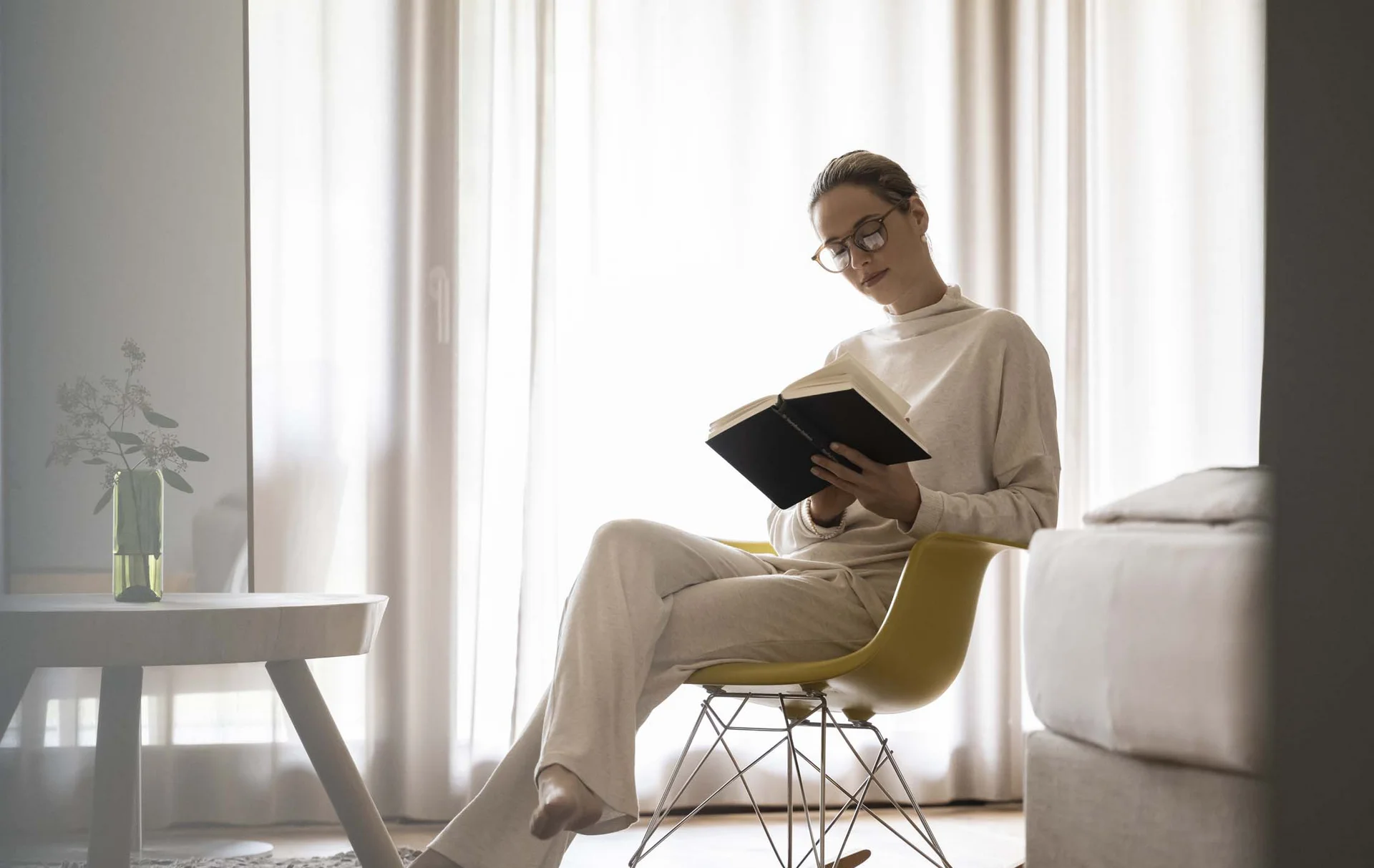 Woman reading a book while sitting on a yellow rocking chair in the living room