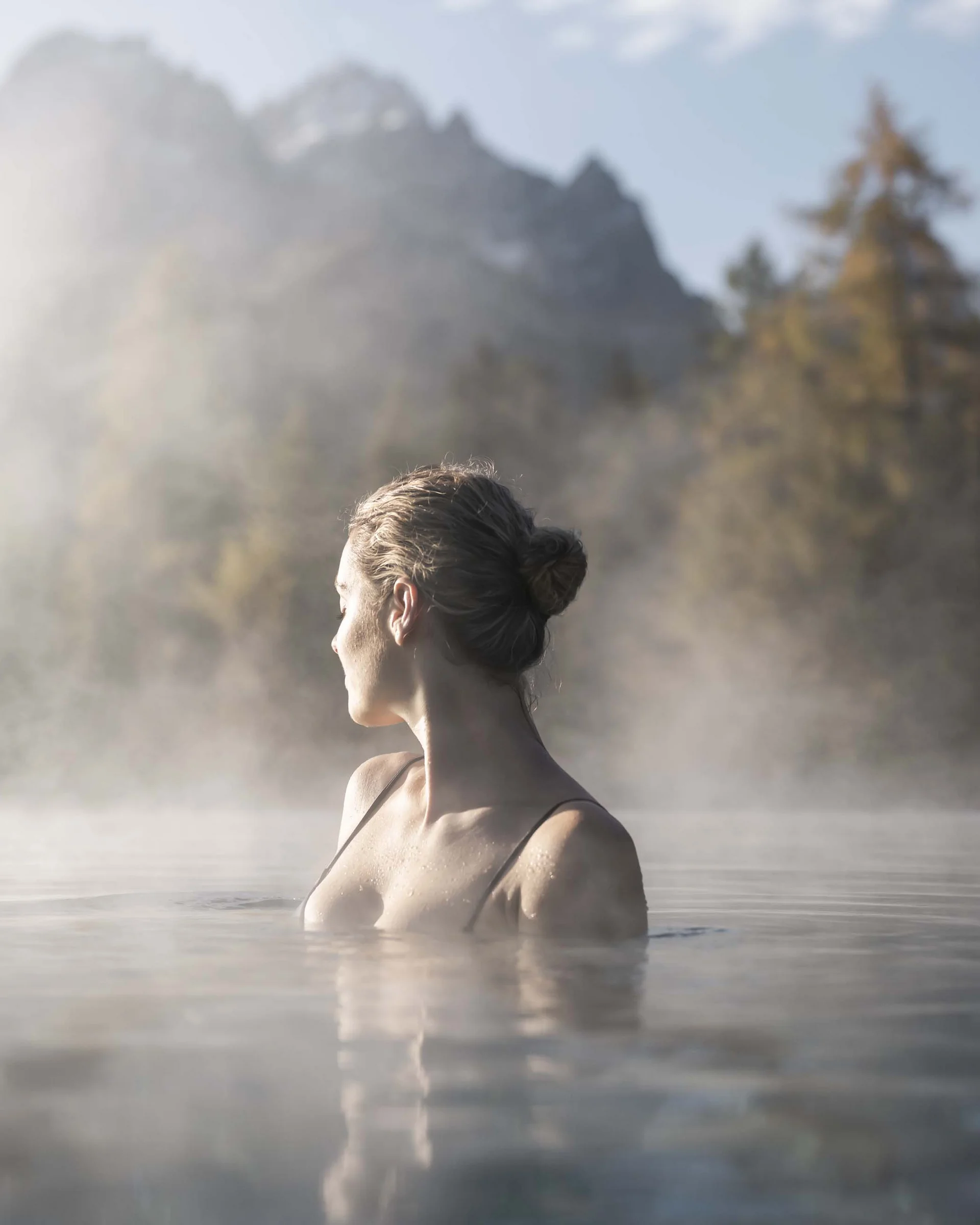 Frau entspannt im heißen Thermalwasser mit nebeligem Bergpanorama im Hintergrund