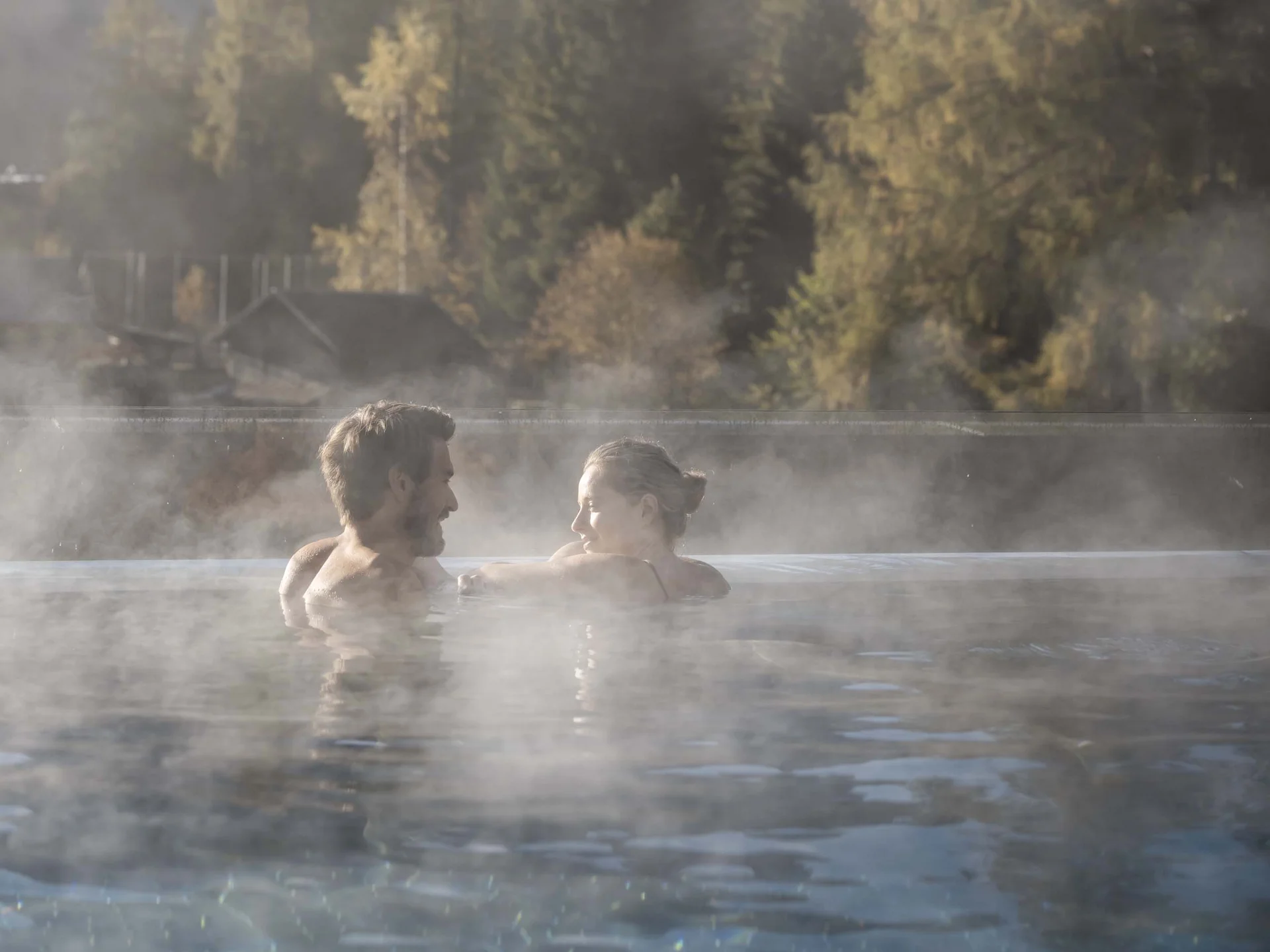 Hotel Monika: das romantische Hotel in Südtirol Paar entspannt im dampfenden Außenpool vor Bergkulisse