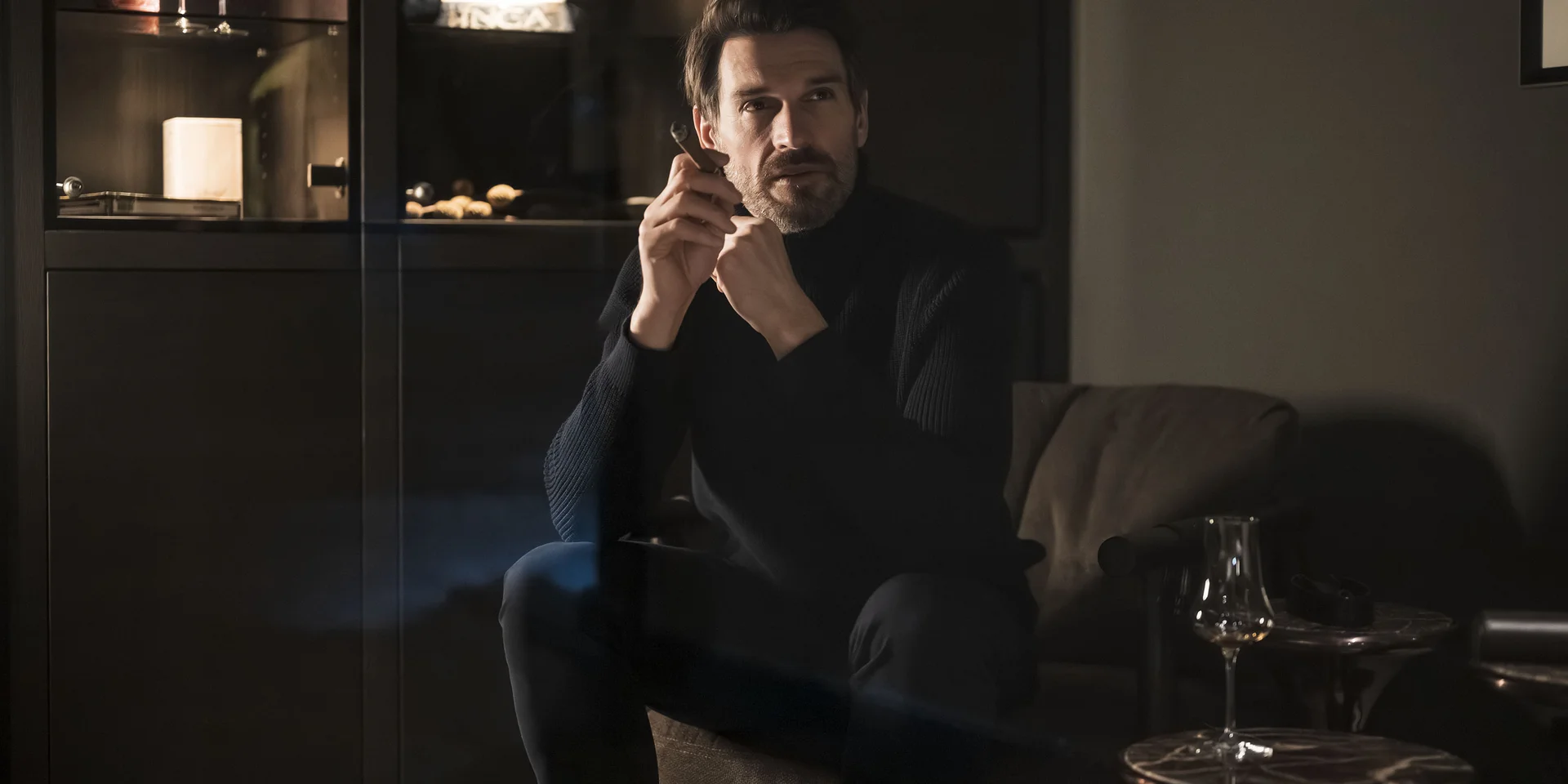 Uomo con maglione scuro seduto pensieroso in stanza accogliente