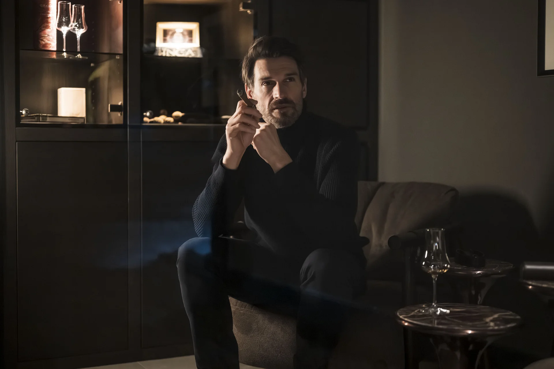 Mann in dunklem Pullover sitzt nachdenklich in gemütlichem Raum