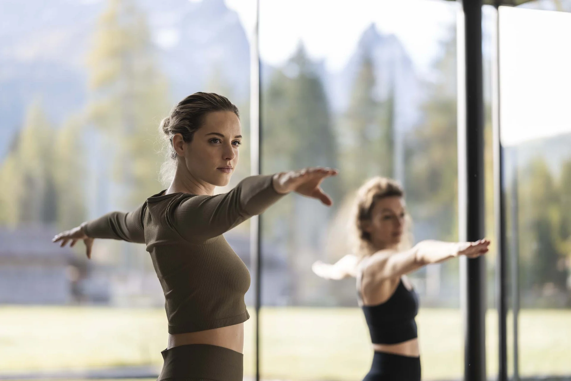 Zwei Frauen machen Yoga-Übung mit ausgestreckten Armen in hellem Raum