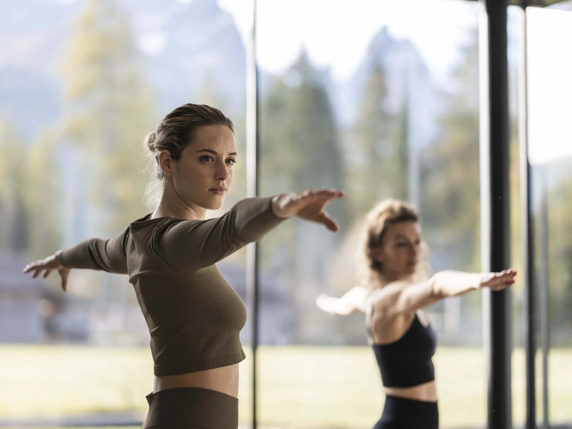 Fitness, Yoga, Outdoor-Erlebnisse: Aktivhotel in Südtirol Zwei Frauen machen Yoga-Übung mit ausgestreckten Armen in hellem Raum