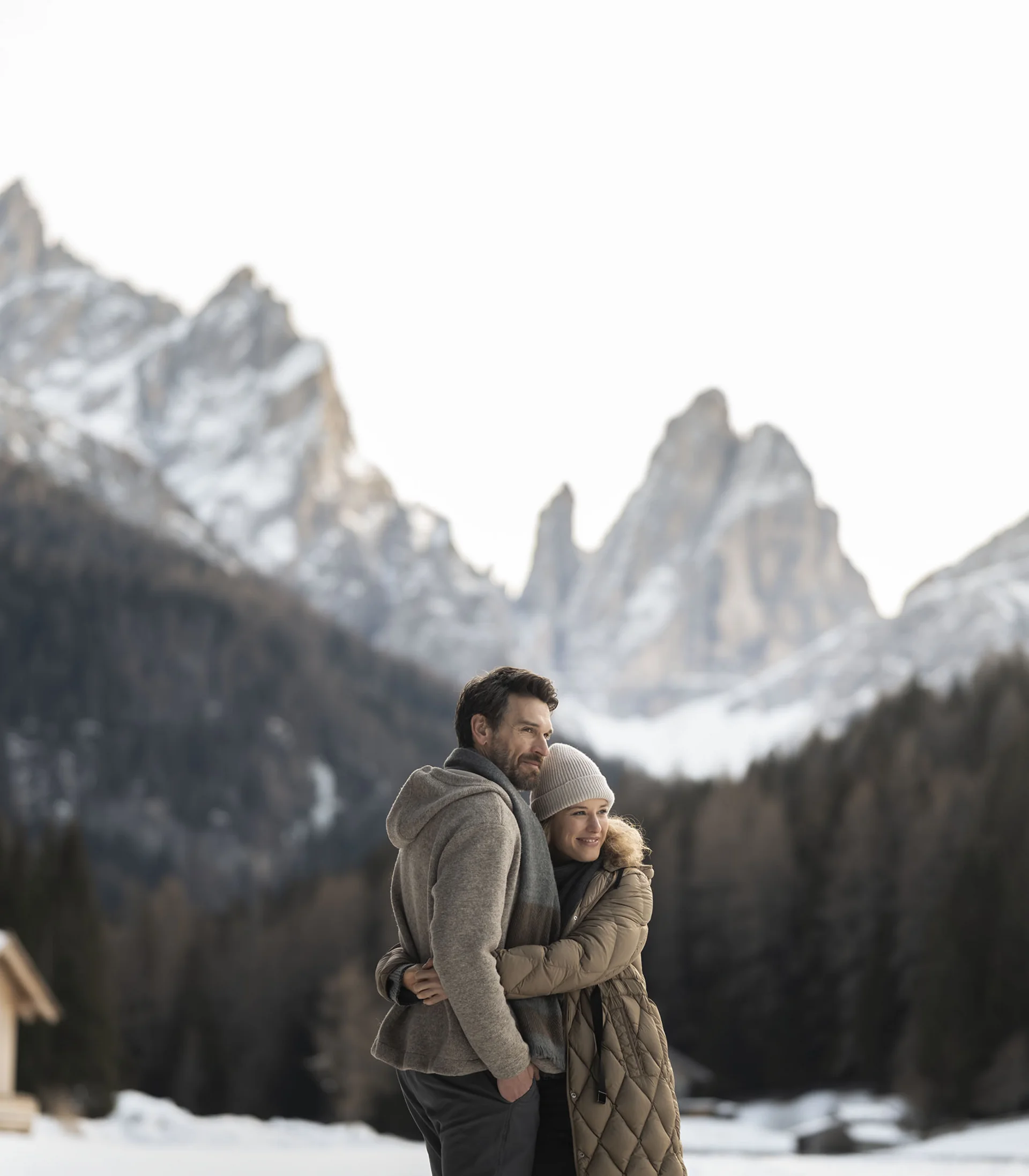 Coppia che si abbraccia sulla neve davanti a montagne e baite innevate