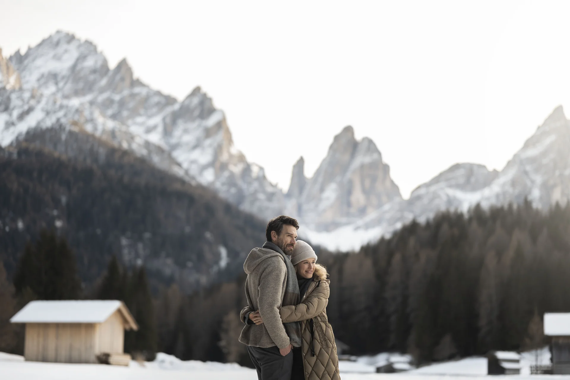 Paar umarmt sich im Schnee vor verschneiten Bergen und Hütten