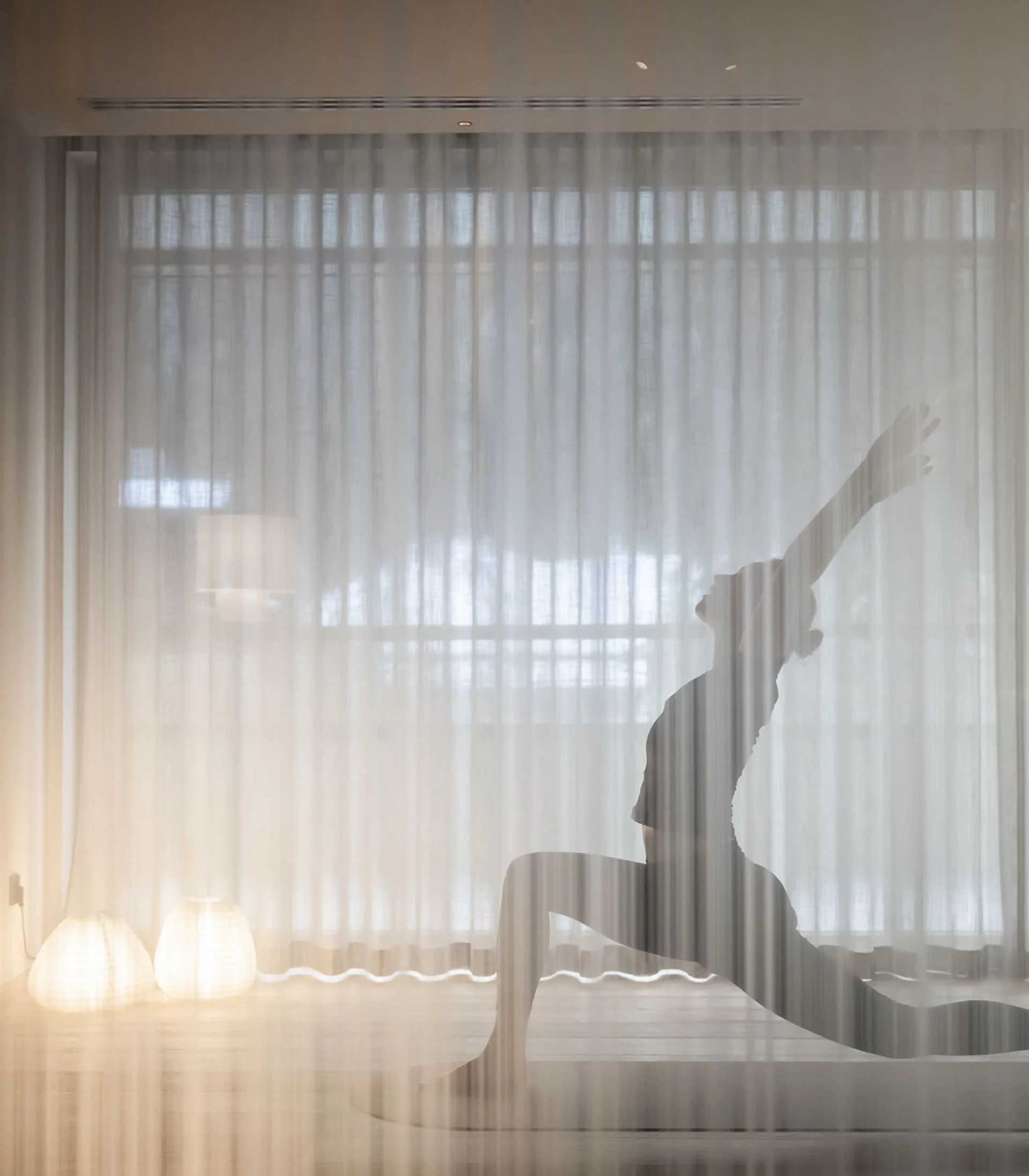 Persona che pratica yoga in posizione del guerriero dietro una tenda traslucida