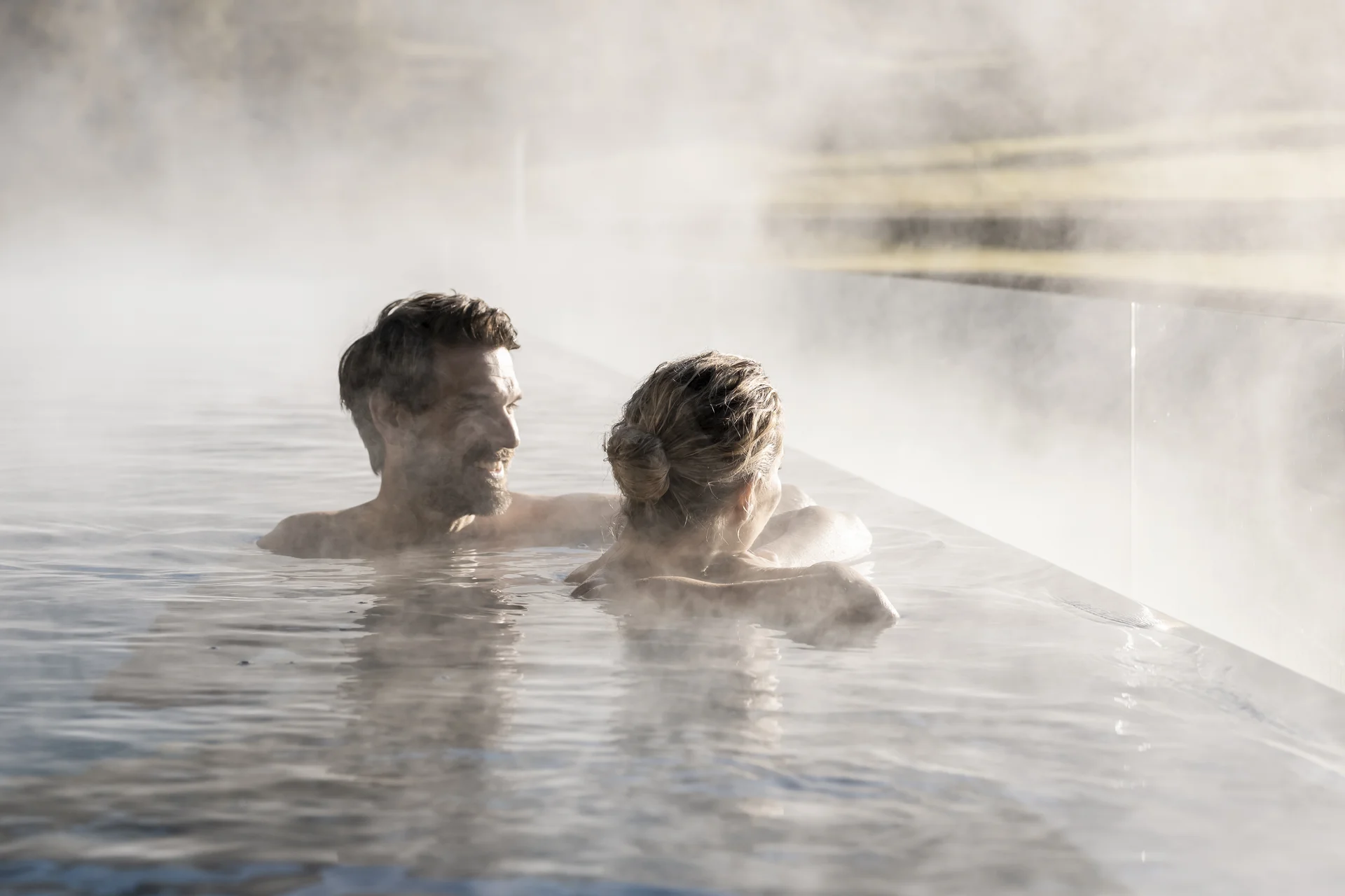 Two people enjoy a heated outdoor pool with steam in a mountain setting