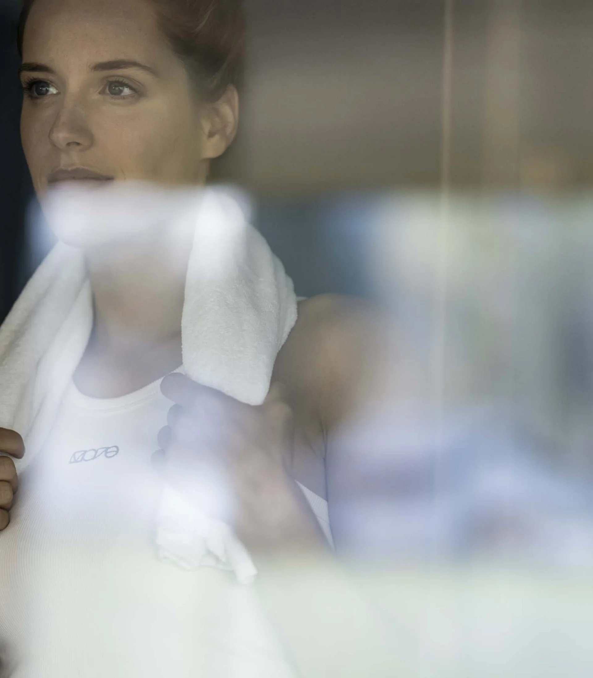 Frau mit Handtuch nach dem Training blickt nachdenklich durch Fenster